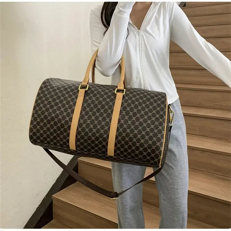 Woman holding a dark patterned travel duffel bag with tan handles and shoulder strap.