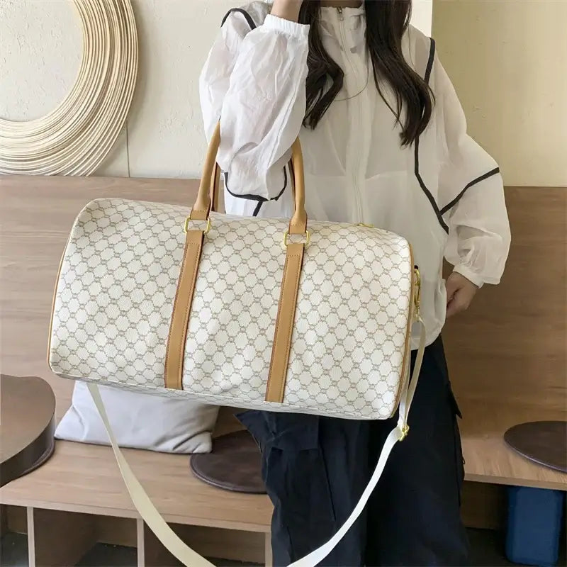 Woman carrying a large beige patterned travel duffel bag with tan handles.