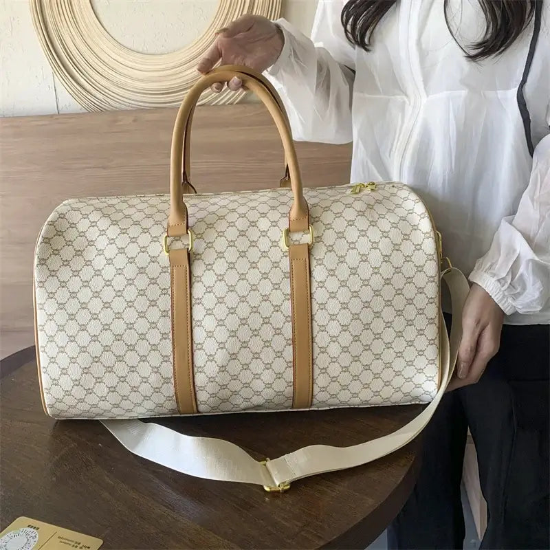 Woman carrying a large beige patterned travel duffel bag with tan handles.