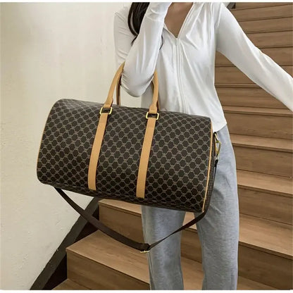 Woman holding a dark patterned travel duffel bag with tan handles and shoulder strap.