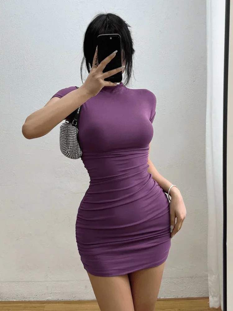 Woman wearing a fitted purple ruched mini dress with short sleeves.